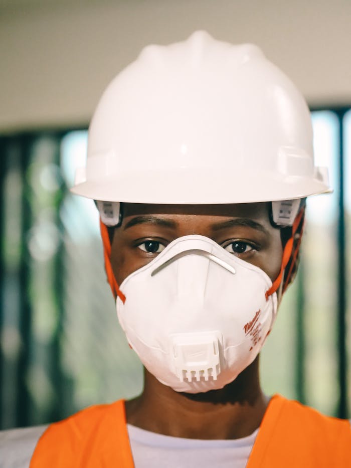 pexels photo 8487784 Close-up of a construction worker wearing a white hardhat and N95 mask indoors.