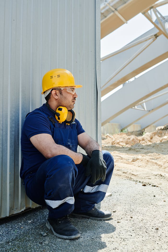 why-choose-us Worker in safety gear sits on site taking a break. Outdoor industrial setting.